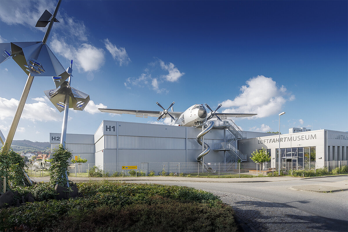 Große Hallen der Hangars H1 und H2 sowie Cafeteria von außen mit begehbarer Transall auf dem Dach und Riesenrutsche nach unten