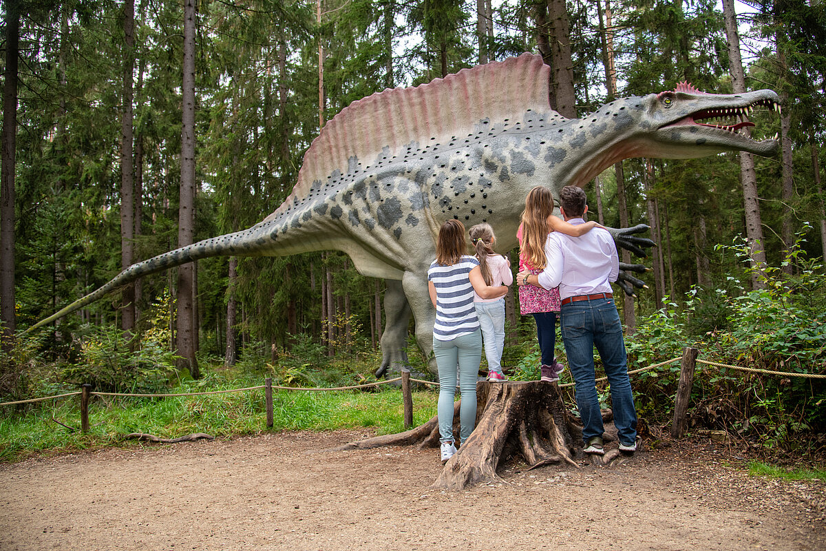 Eine Famile steht vor einer Dinosaurierfigur im Wald