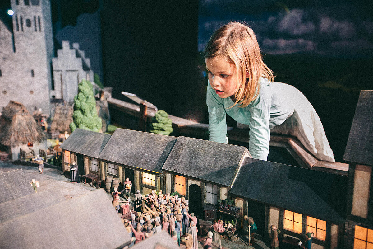 Ein Mädchen schaut staunend auf die Kulisse einer Miniatur-Dorfgemeinschaft