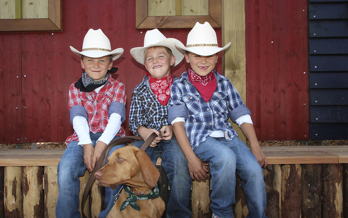 Drei Jungs sitzen in Corboy-Outfits auf einer Veranda