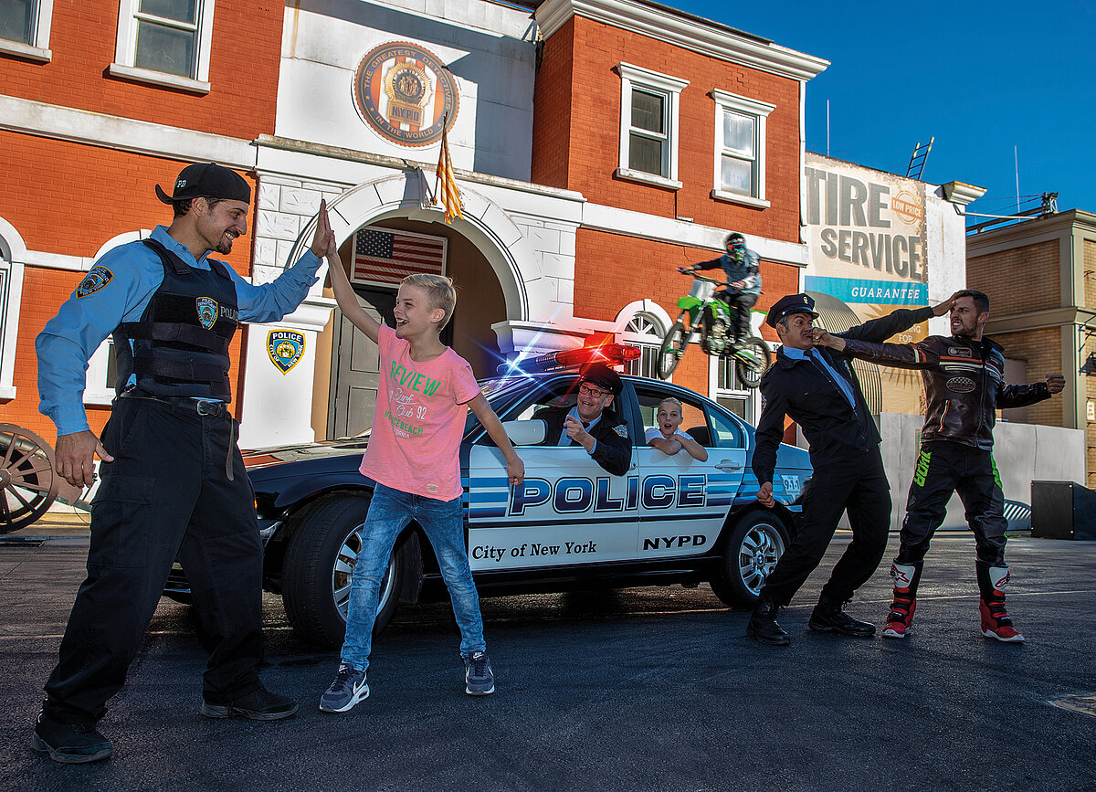 Ein Kind schlägt in einer Stunt-Show mit einem amerikanischen Cop ein. Hinter den beiden fährt ein Polizeitauto, ein Cop und ein krimineller kämpfen und ein BMX-Bike fliegt durch die Luft. 