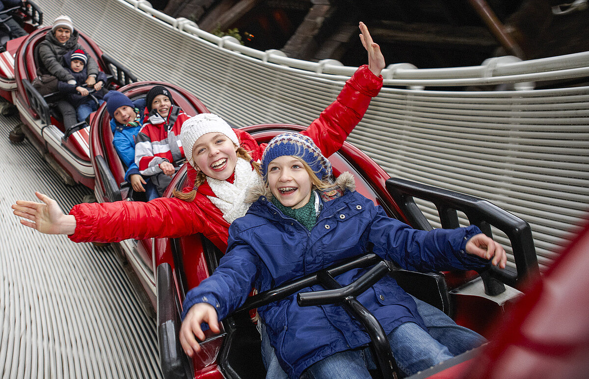 Kinder in Winterkleidung fahren in kleinen Achterbahn. Ein Kind trägt ein Weihnachtsmann-Kostüm.