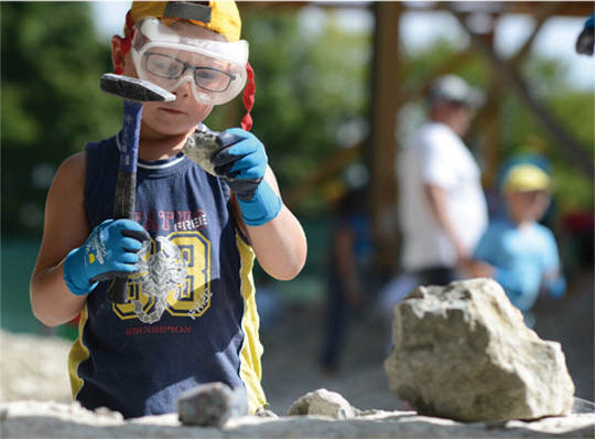 Ein Junge klopft mit einer Schutzbrille eine versteinerte Fossilie aus dem Stein.