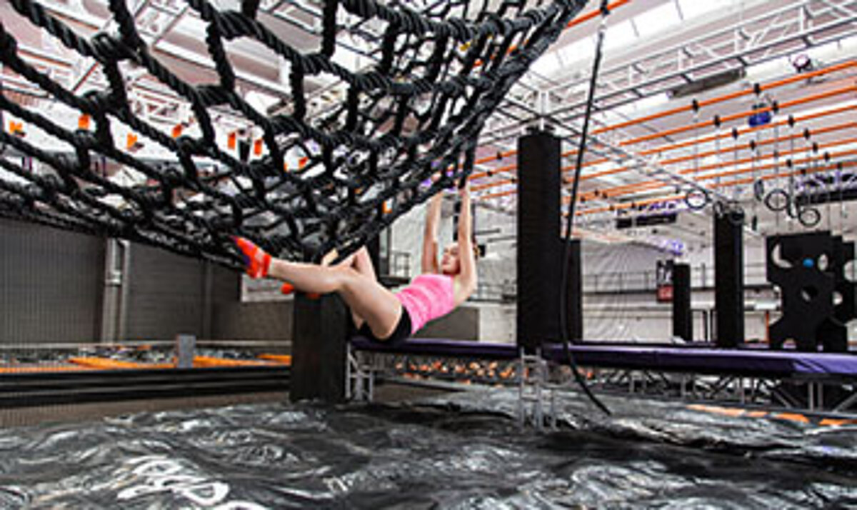 Ein Mädchen hangelt an einem Netz über einem großen Trampolin