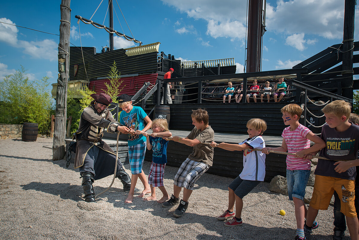 Ein Pirat ist beim Tauziehen mit mehreren Kindern im Sandaksten vor einem Piratenschiff