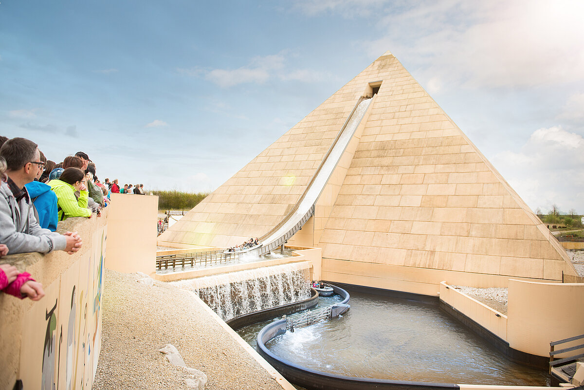 Eine große Pyramide aus der eine lange Rutsche runter führt wird von Besuchern bestaunt