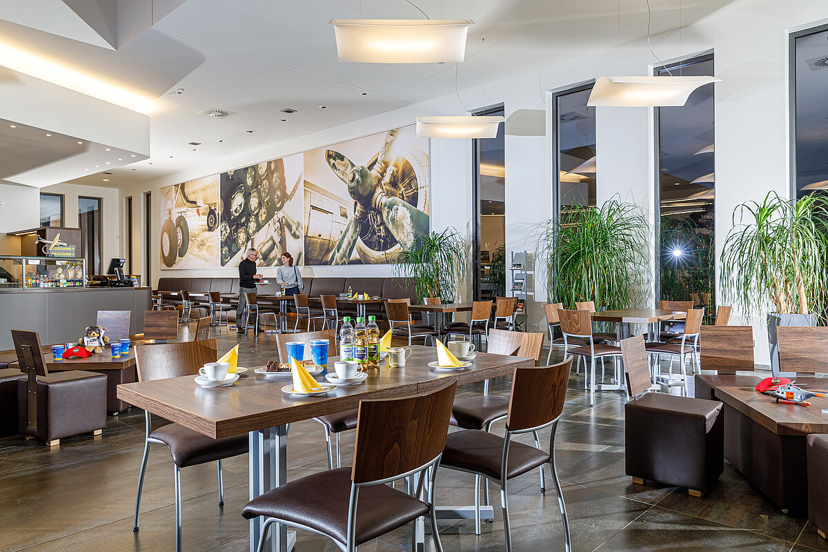 Cafeteria mit moderner Einrichtung, großformatigen Flugzeugmotiven an den Wänden und Selbstbedienungstresen im Hintergrund