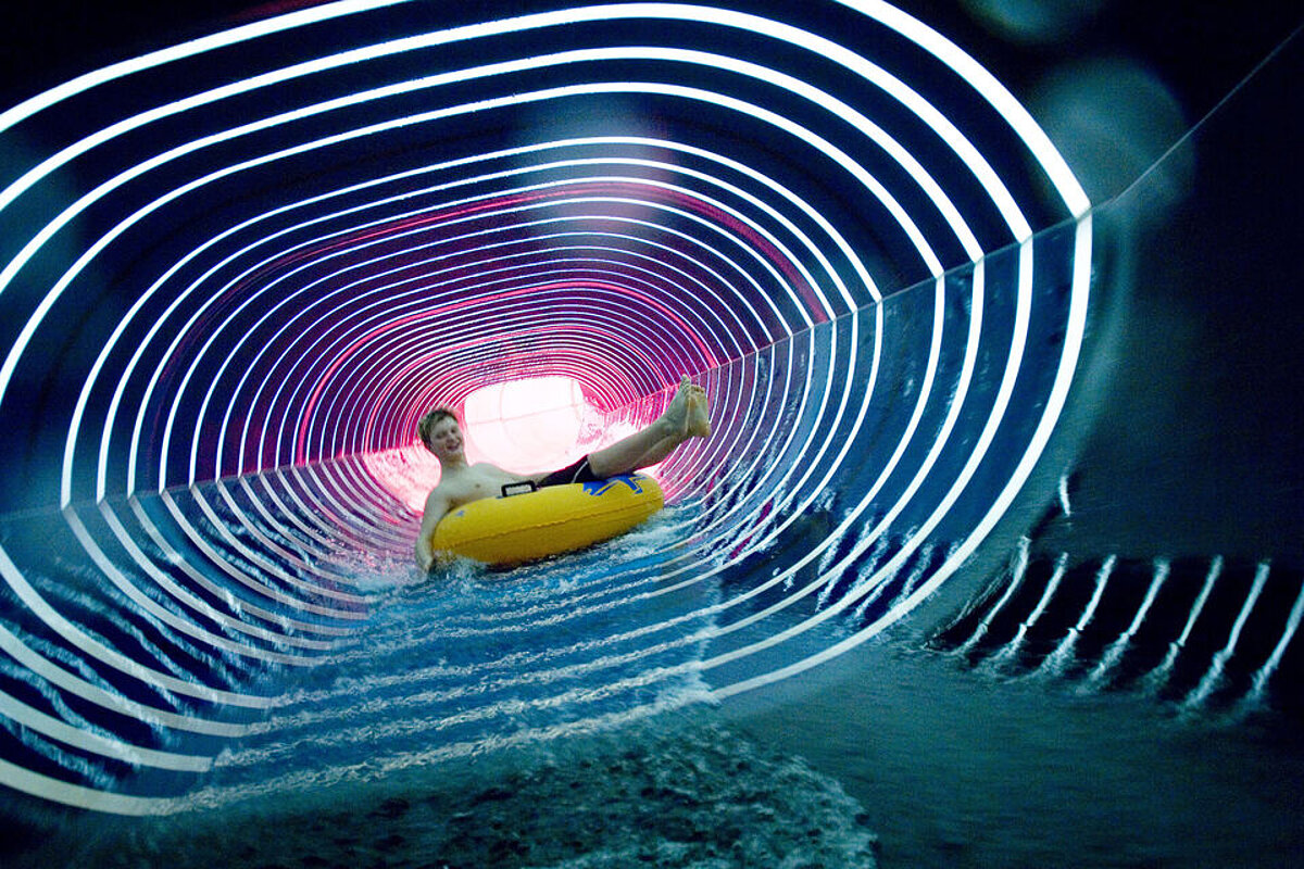 Ein Mann rutscht in einem futuristischen Tunnel im Badeparadies auf einem Reifen
