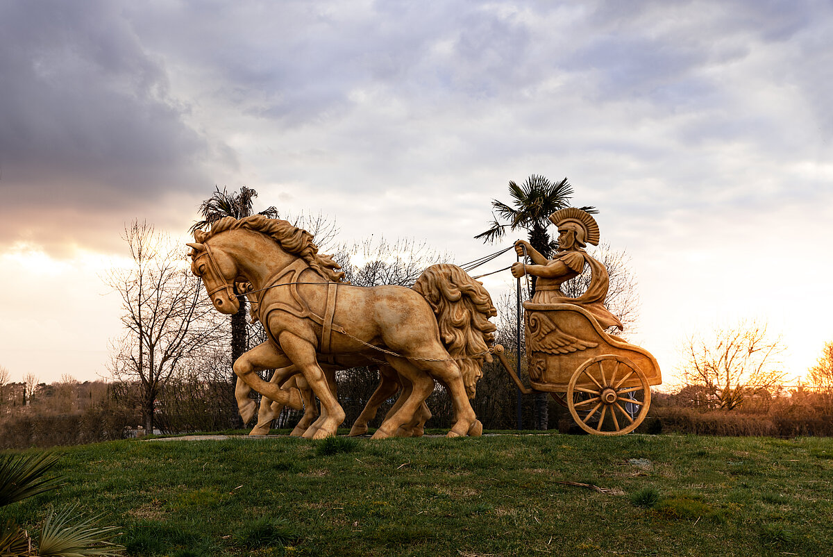 Die Figur eines Römers der vor untergehender Sonne auf einem Pferdewagen gezogen wird