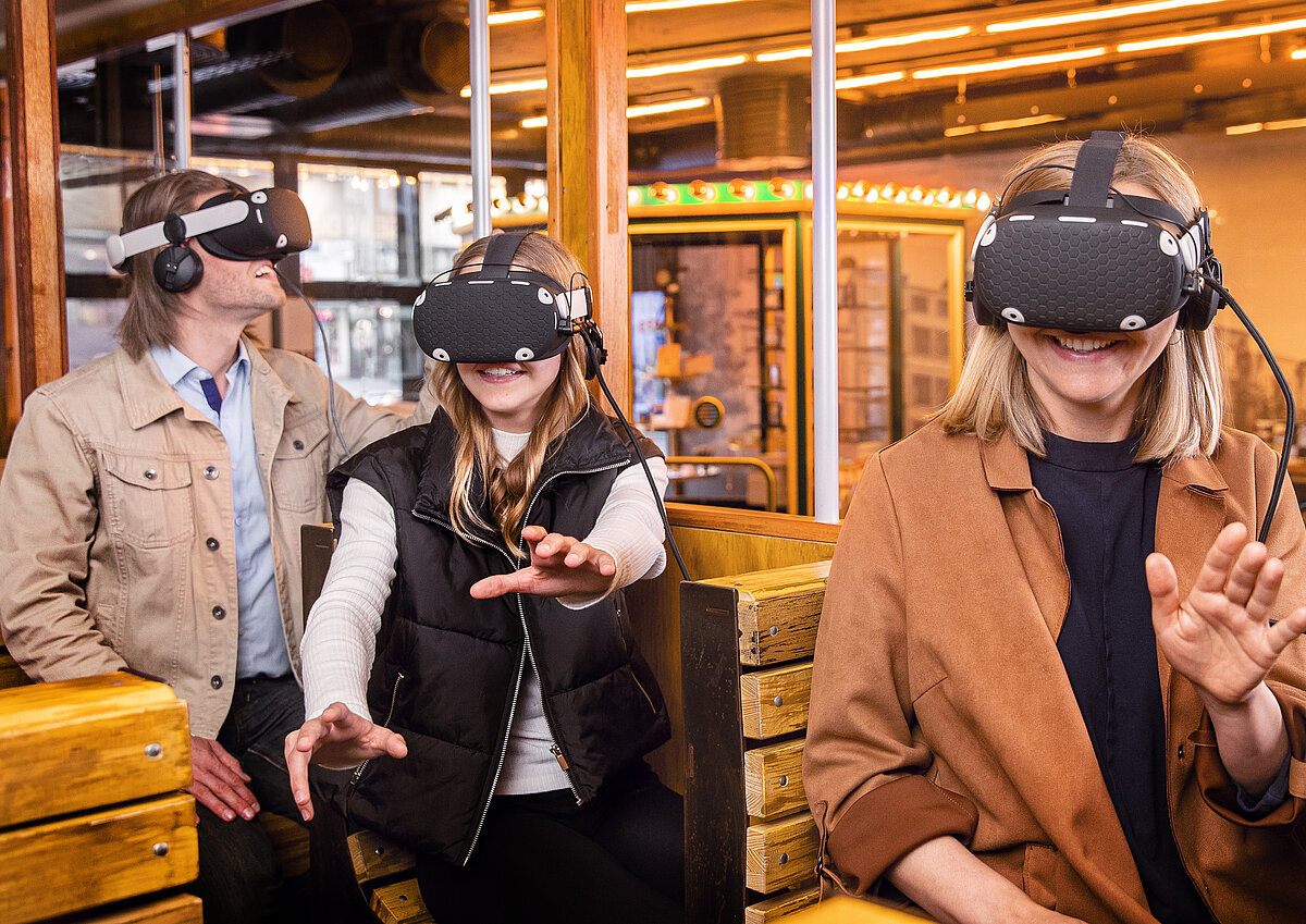 Drei Gäste in einer alten Trag, die sich bewegen, als wären sie wirklich in der virtuellen Welt, die sie über die VR-Brillen sehen.